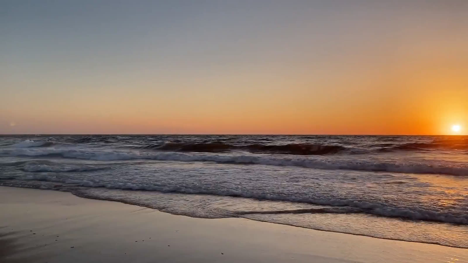 Surf rolling onto a Pacific beach at sunset